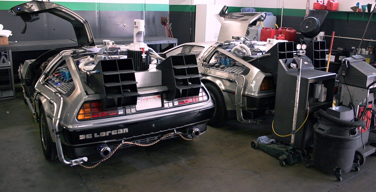 Two DeLorean time machine replicas parked side by side in a garage, gull-wing doors open
