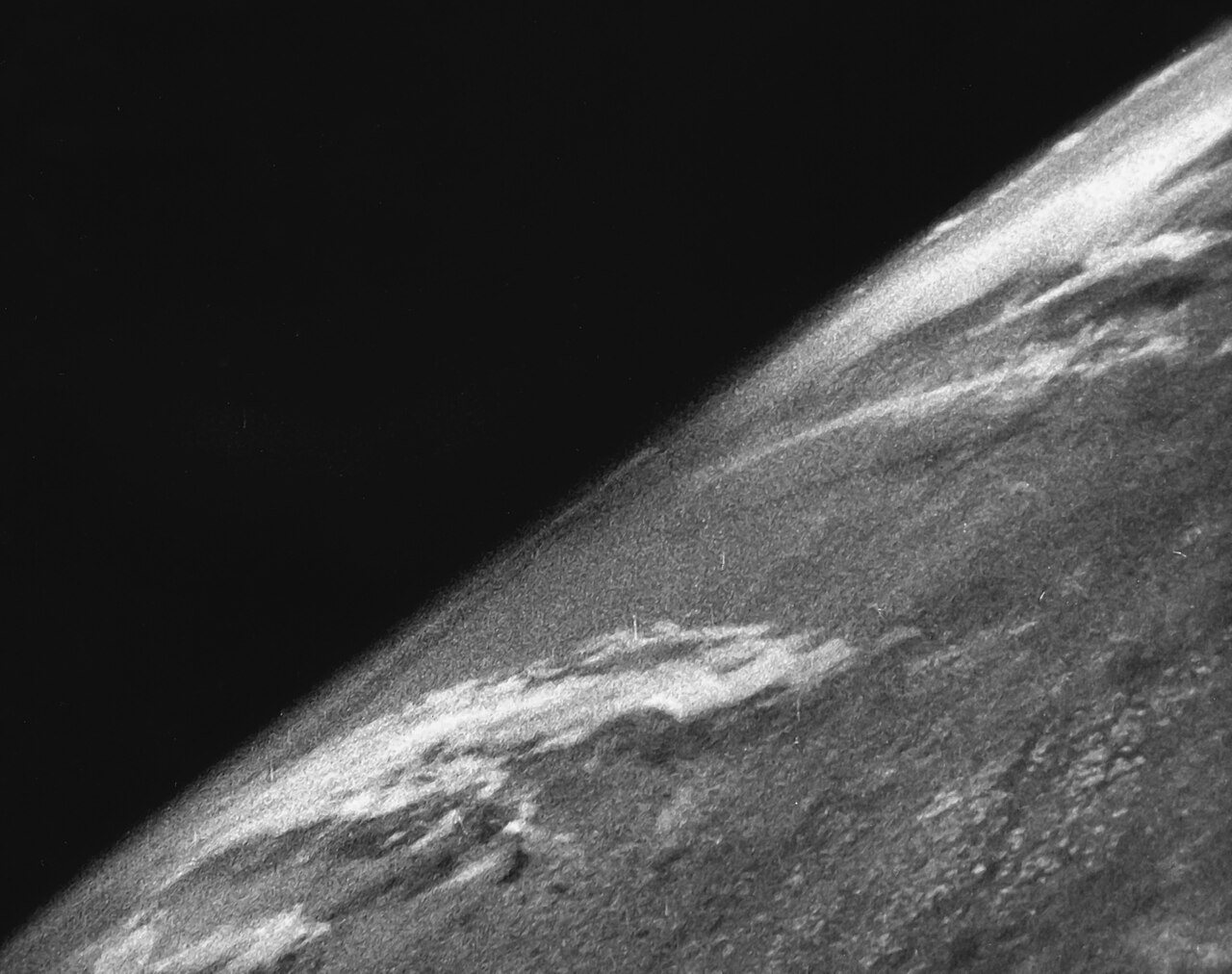 Black and white photo of the curved edge of the Earth with clouds below and the black sky of space above, taken from a V-2 rocket in 1946